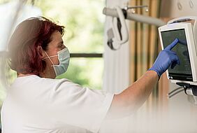 Mitarbeiterin der Pflege mit Mund-Nasen-Schutz liest am Bildschirm Daten ab